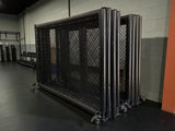 Cage MMA pliable repliée en deux trains de panneaux, rangée le long d'un mur sur ses roulettes