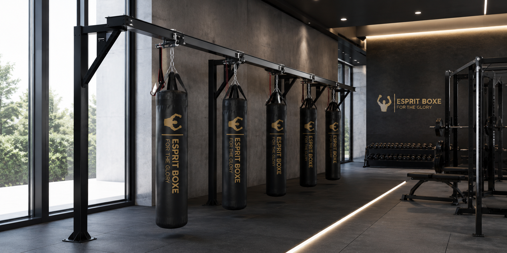 Collection rails de convoyage pour sac de frappe Esprit Boxe : rail acier noir suspendu sur poteaux à potence, cinq sacs de frappe noirs à logo doré For the Glory accrochés par chariots coulissants, chaînes et sangles, dans une salle vitrée