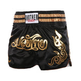 Short muay-thaï noir à lettrage thaï มวยไทย brodé or, ceinture à deux bandes dorées, vue de face
